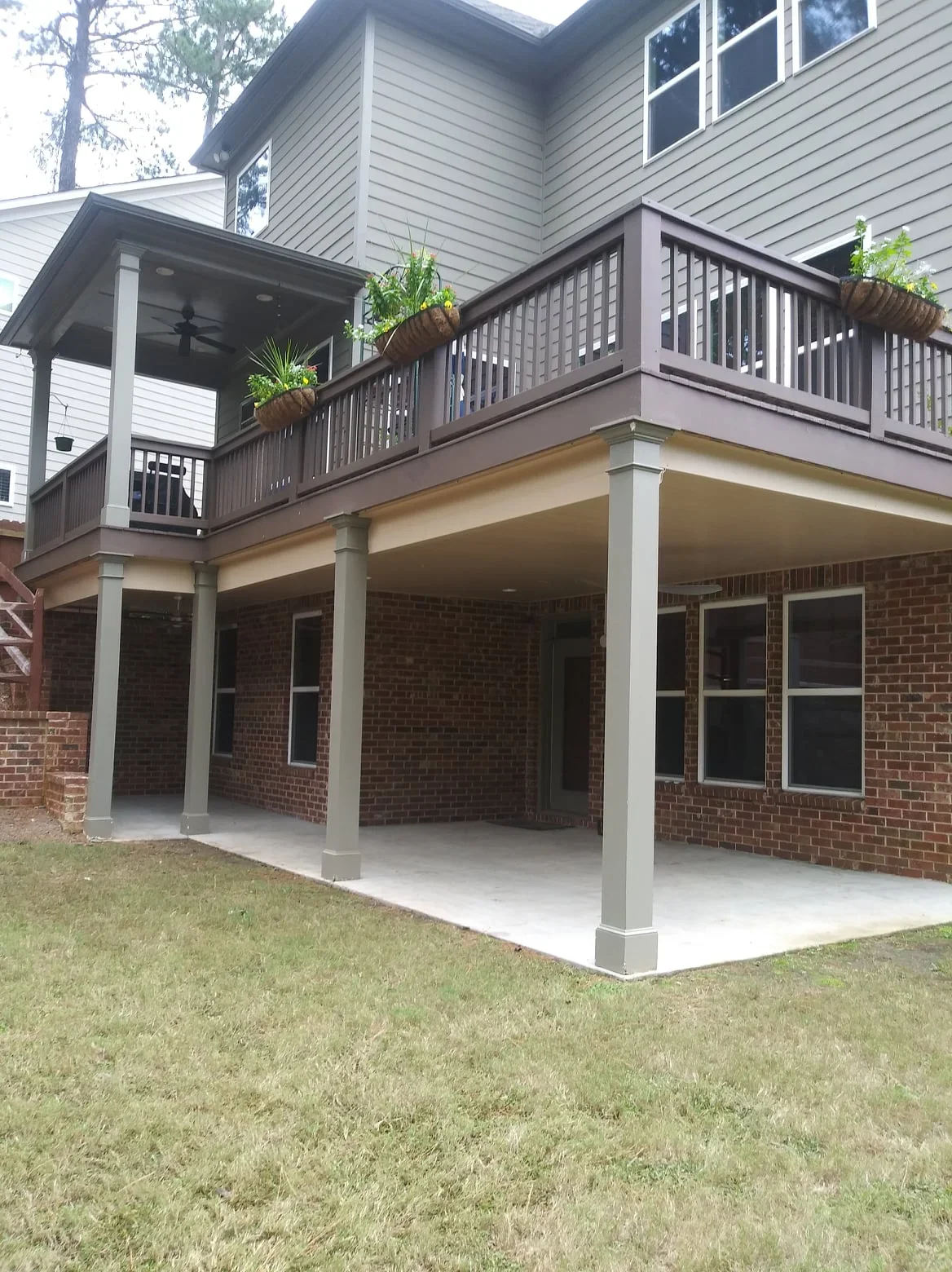 Waterproof under-deck system with gray posts and concrete pad beneath elevated composite deck with screened room
