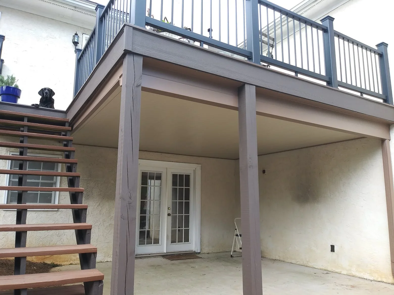 Gray composite under-deck system with finished ceiling beneath elevated deck and metal railings