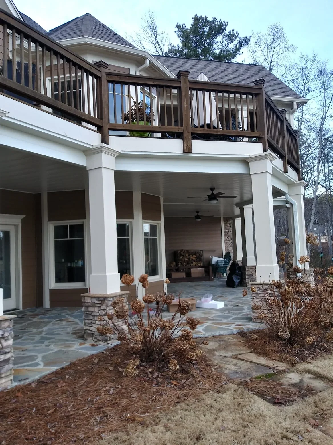 Two-story deck with dark aluminum railings above covered patio with under-deck drainage system and stone flooring