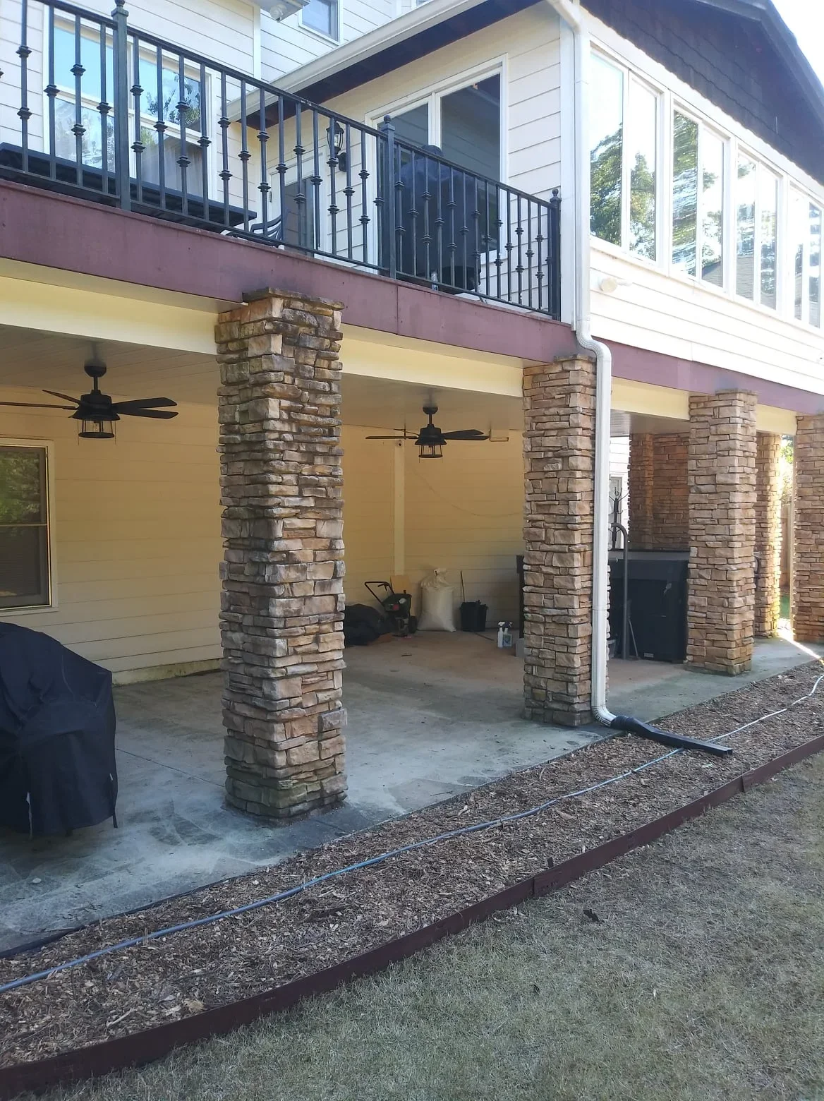 Yellow patio cover with brick columns, black ceiling fans, and upper deck with aluminum railing