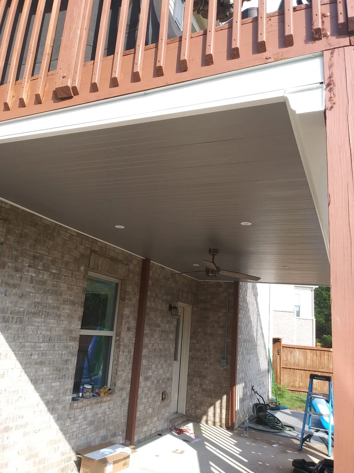 Gray composite under-deck ceiling with recessed lights and ceiling fan over brick patio