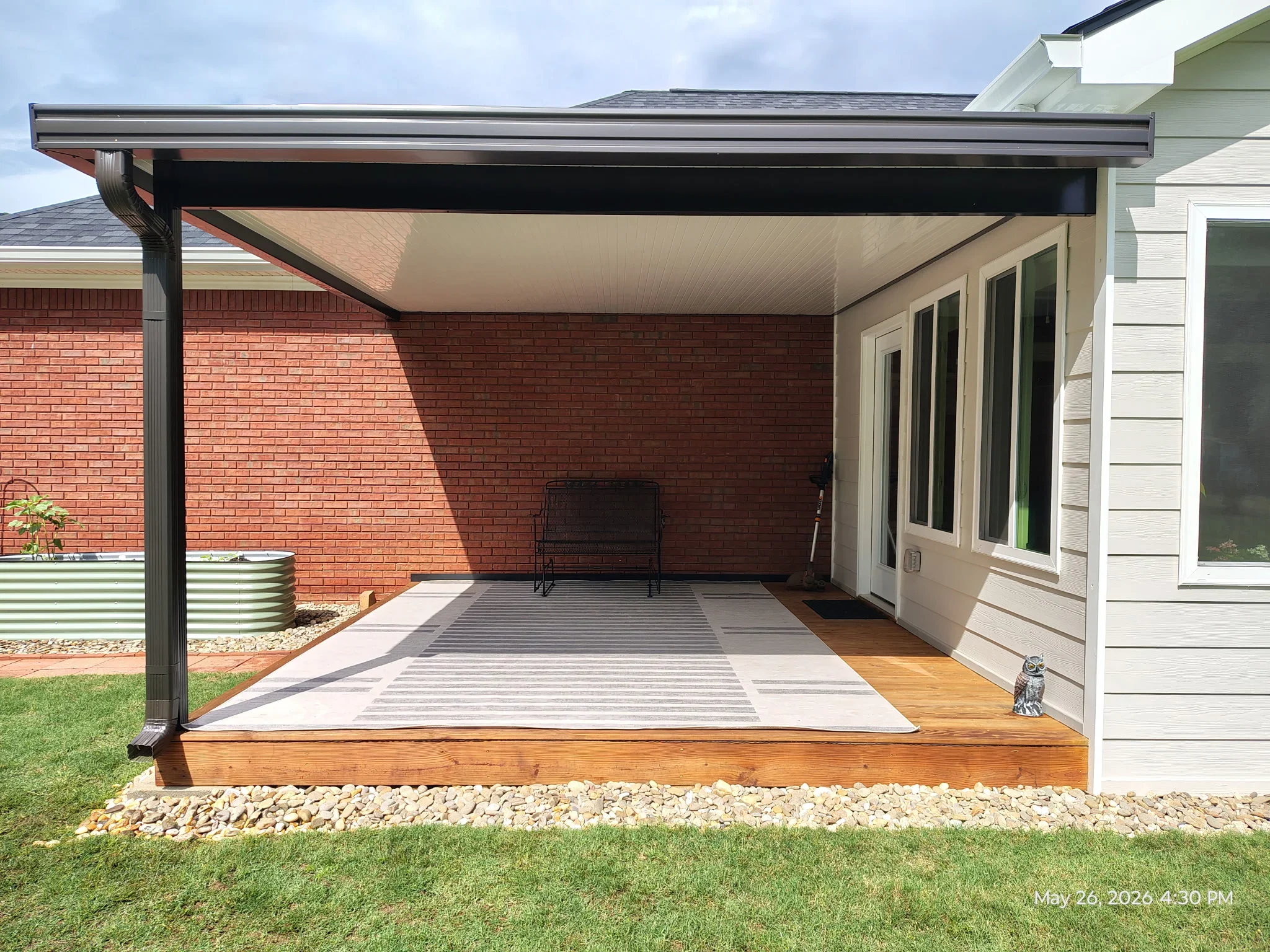 Black aluminum patio cover with cream polycarbonate ceiling over composite deck and brick home