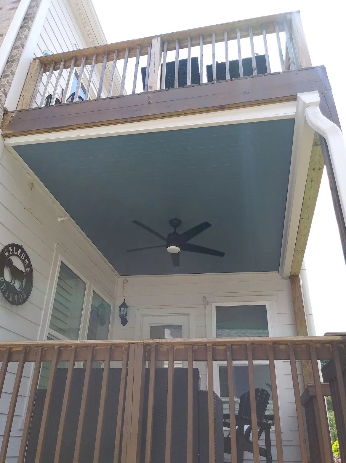 Under-deck waterproofing system with teal ceiling, ceiling fan, and dual-level wood deck railings
