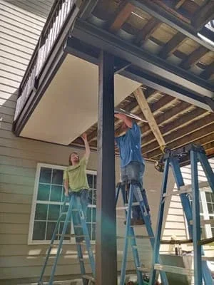Workers installing screen room frame with wooden beams and vertical support posts