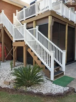Two-story white screen room with deck above, wooden posts, and landscaped entry area