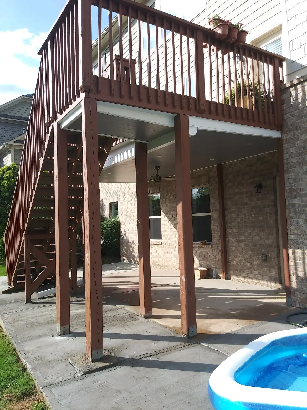 Two-story deck with dark aluminum frame, vertical railings, and under-deck drainage system creating covered patio below