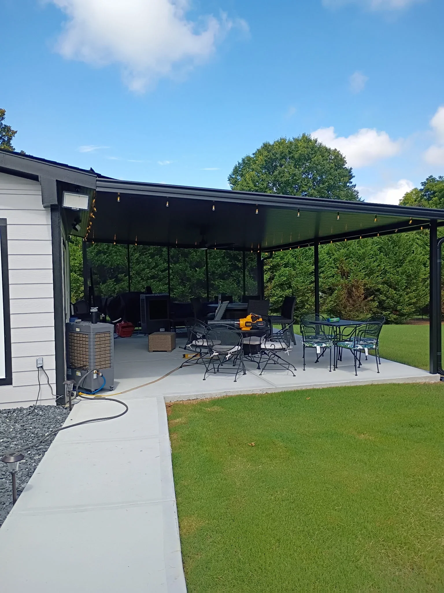 Black aluminum patio cover with retractable shade, pendant lights, concrete pad, and metal furniture