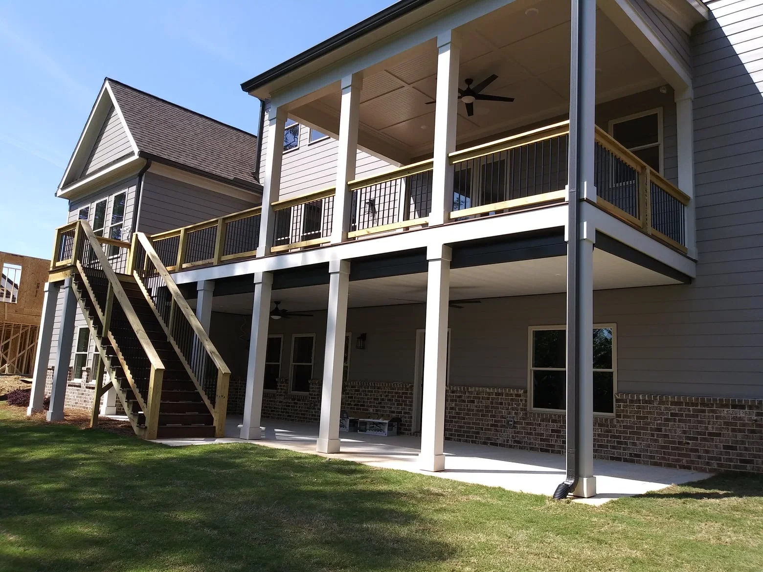 Under-deck ceiling system with white posts, black railings, and integrated lighting on two-story home