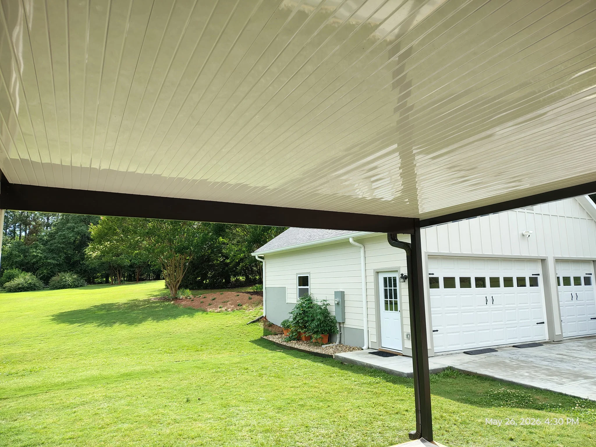 Adjustable louvered aluminum patio cover with dark frame over concrete pad near garage