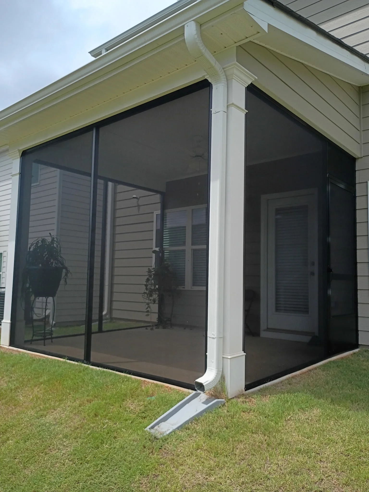 Corner screen room with black aluminum frames, full-height black screening, white trim columns, and cream soffit