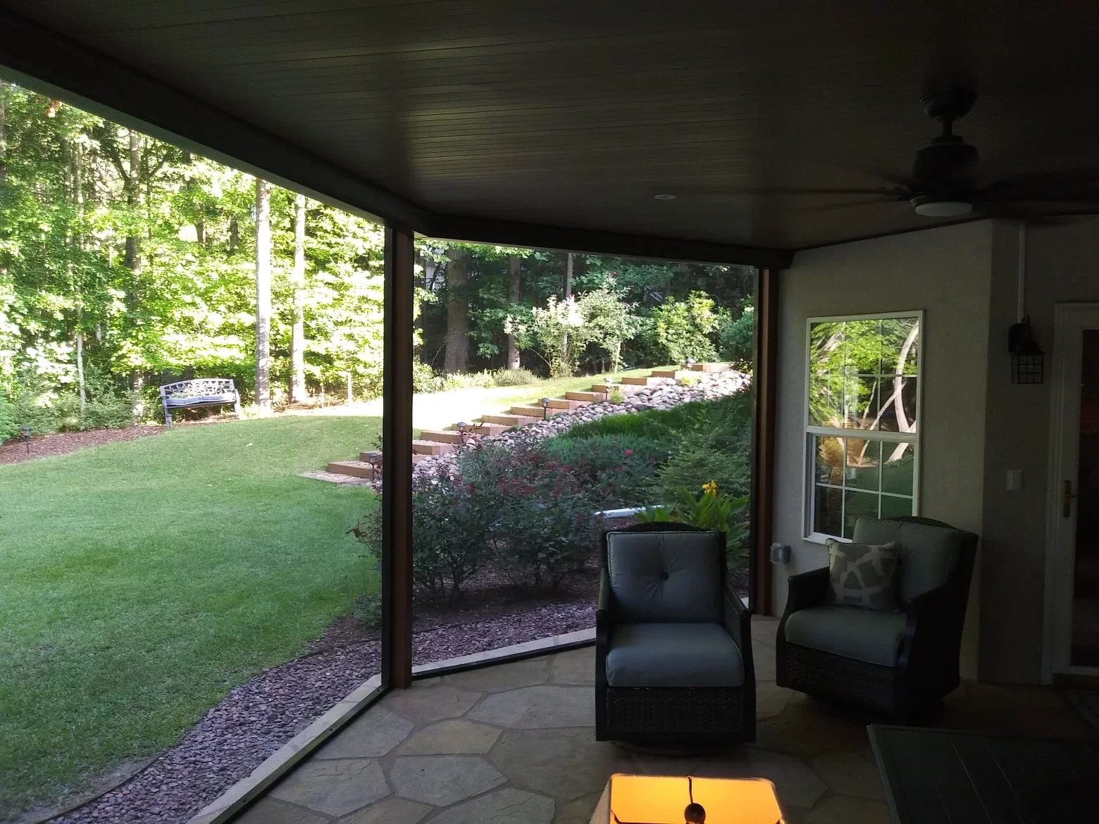Under-deck ceiling with dark finish, glass sliding doors, and screened room overlooking landscaped yard