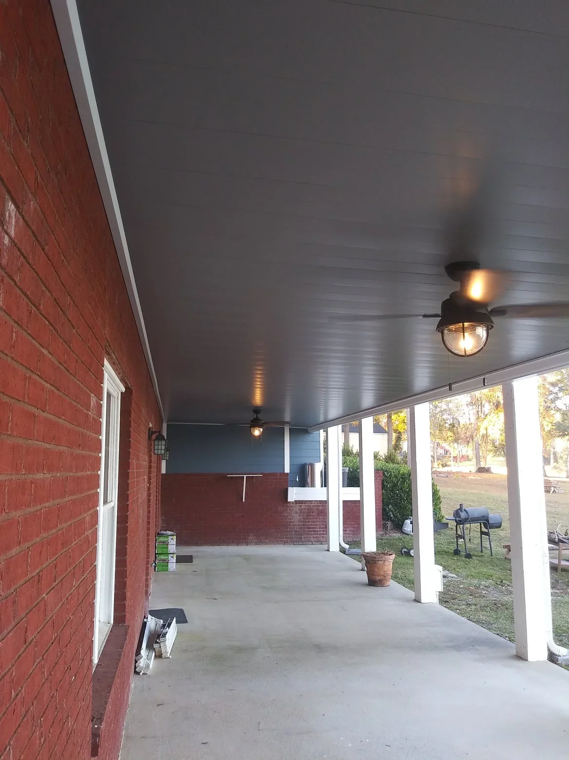 Under-deck system with corrugated metal ceiling, lighting, and ceiling fan installed beneath elevated deck