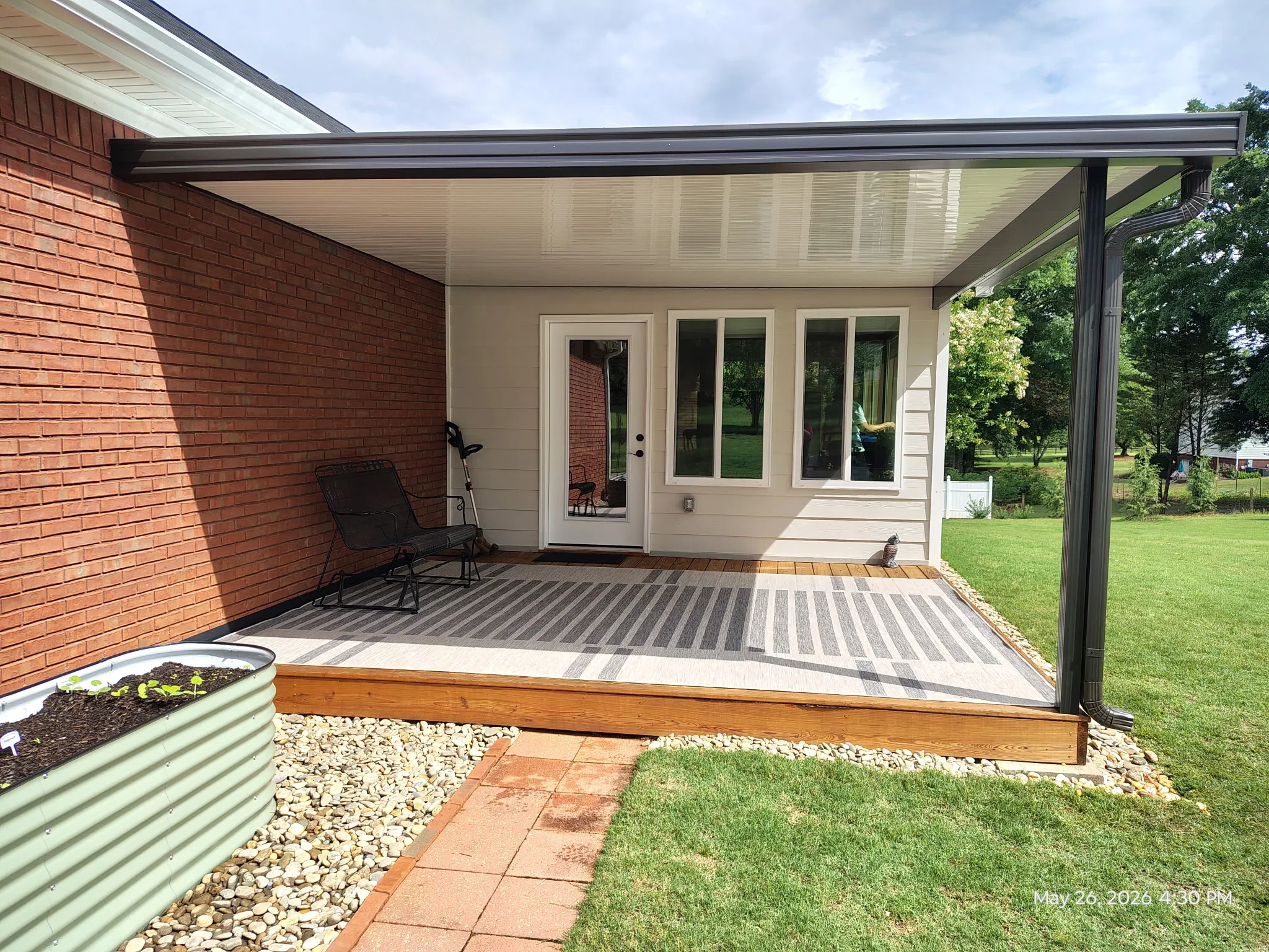 Aluminum patio cover with louvered ceiling over striped composite deck and brick home