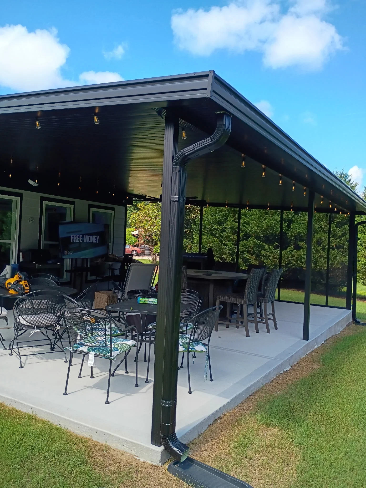 Dark aluminum screen room with full screening, sloped roof, concrete pad, and integrated outdoor furniture area