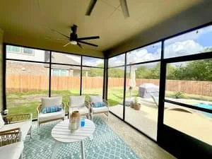 Screened patio room with glass panels, ceiling fan, and pool view in background