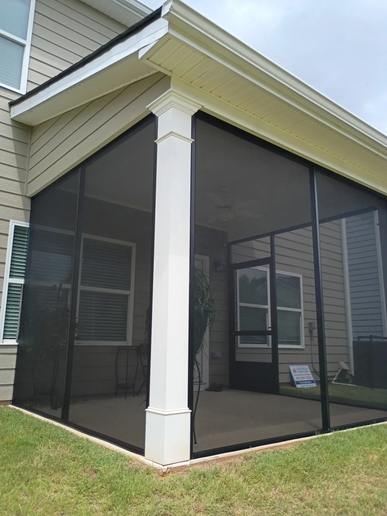 Corner screen room with black mesh panels, white post, and cream soffit trim attached to house