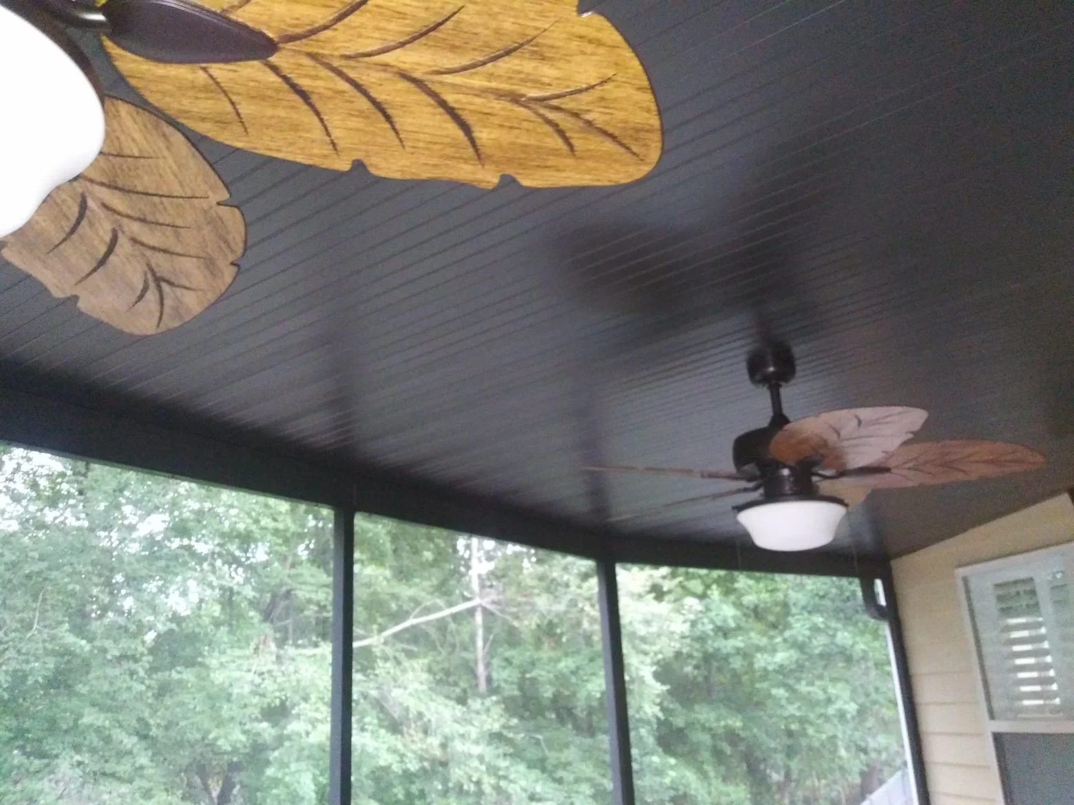 Ceiling fan with wooden leaf blades installed in screened room with dark wood ceiling
