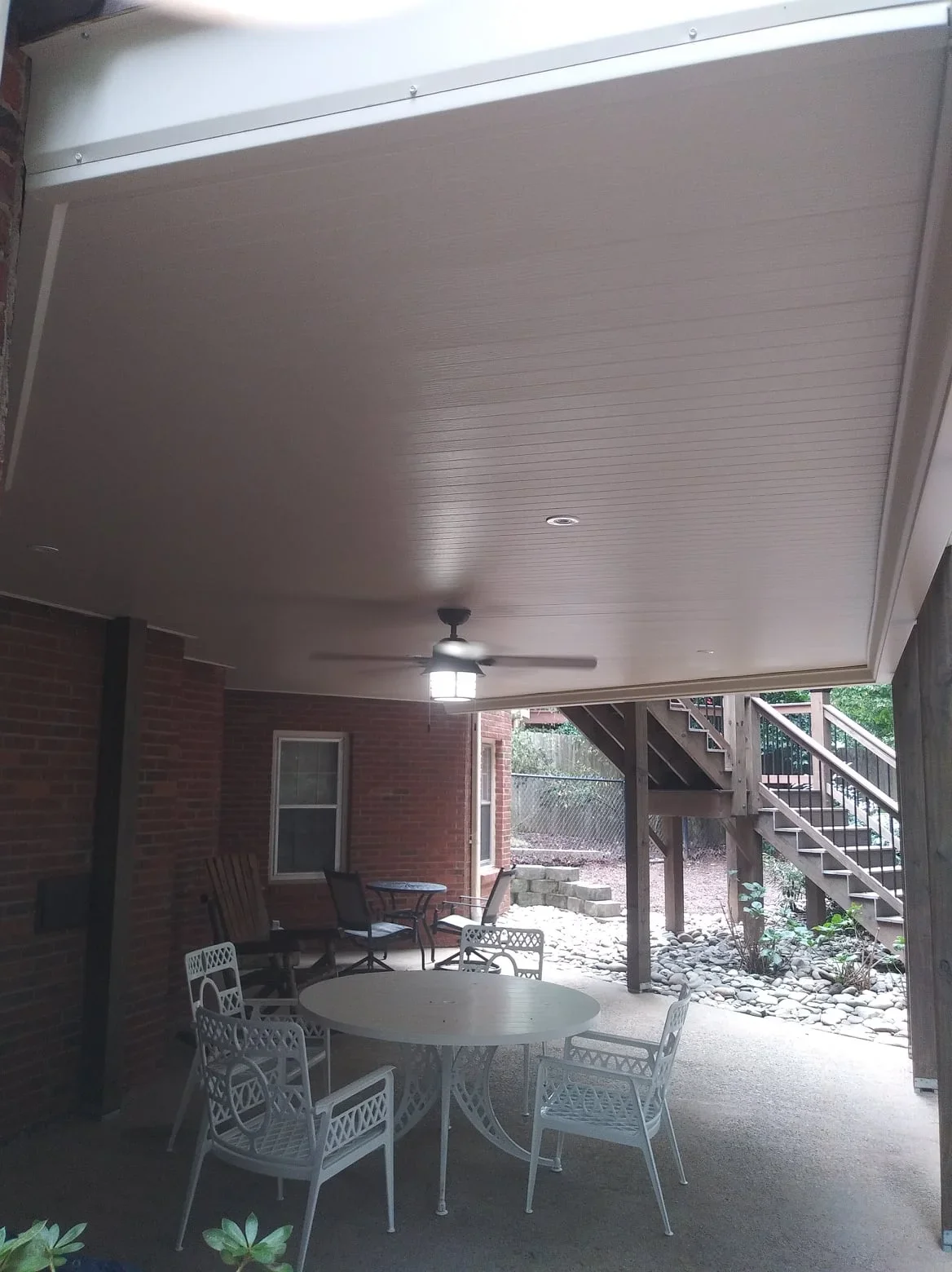 White aluminum under-deck ceiling with recessed lighting and fan installed beneath wooden deck structure
