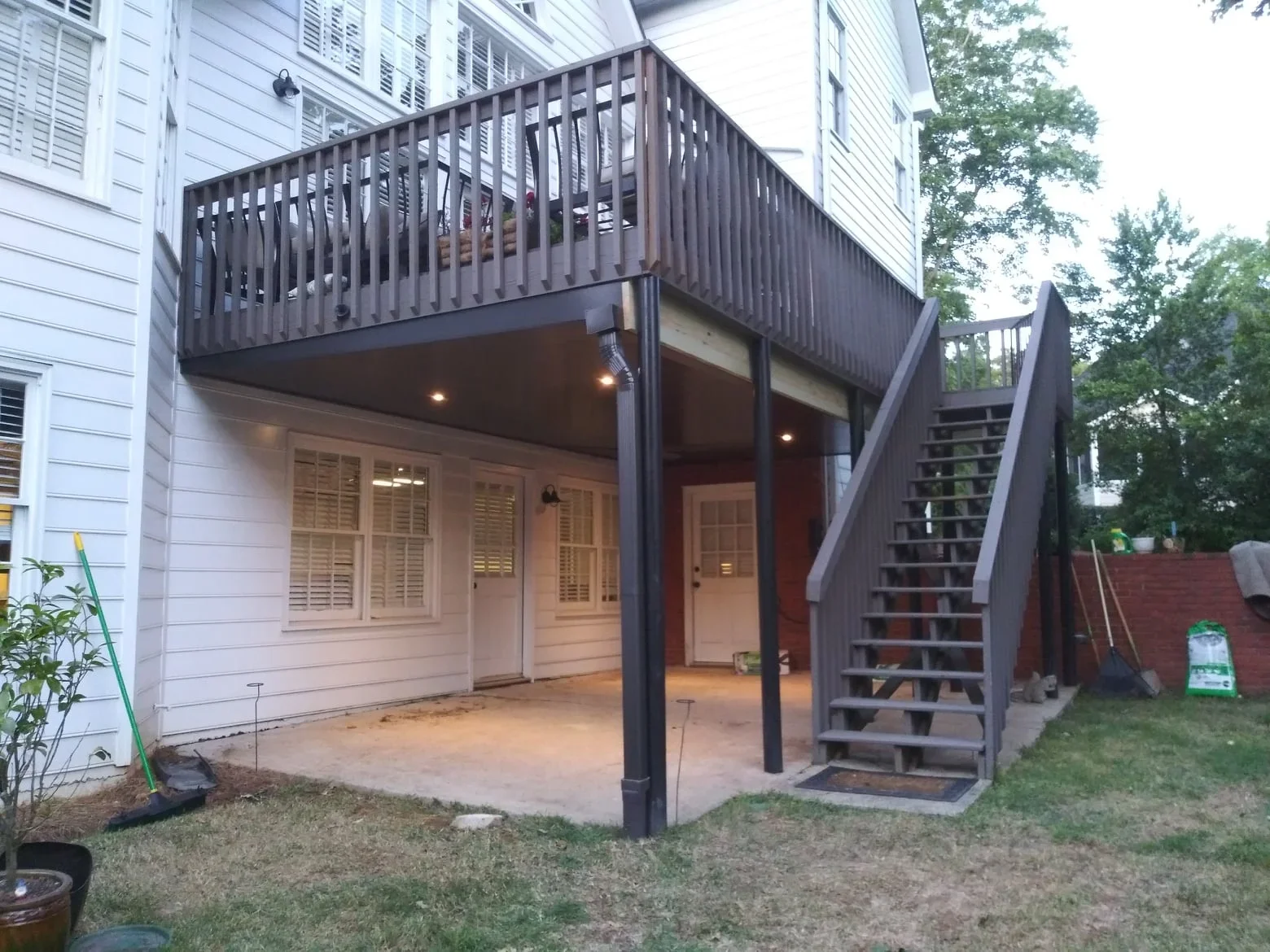Dark metal under-deck system with vertical balusters, recessed lighting, and concrete pad beneath elevated deck