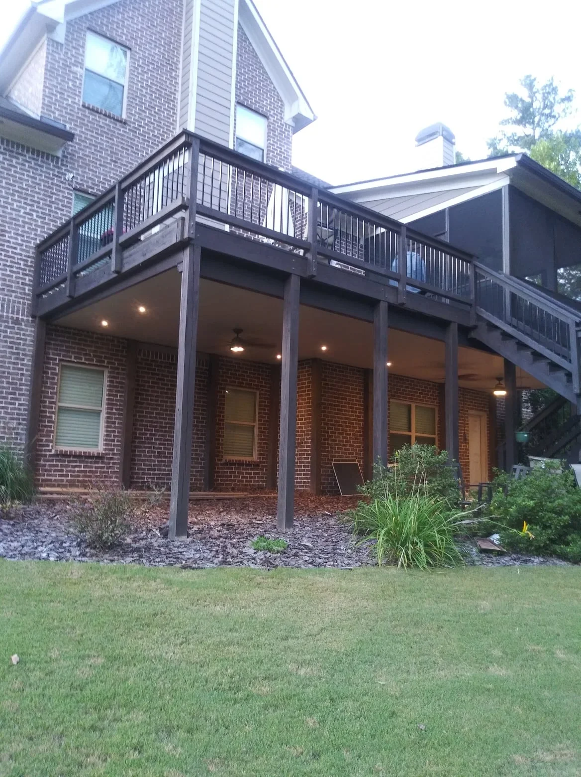 Two-story deck with black metal railings, under-deck system, recessed lighting, and metal roof panels on brick home