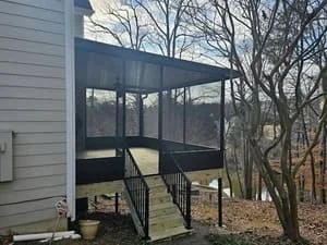 Elevated black-framed screen room with metal railings overlooking wooded backyard