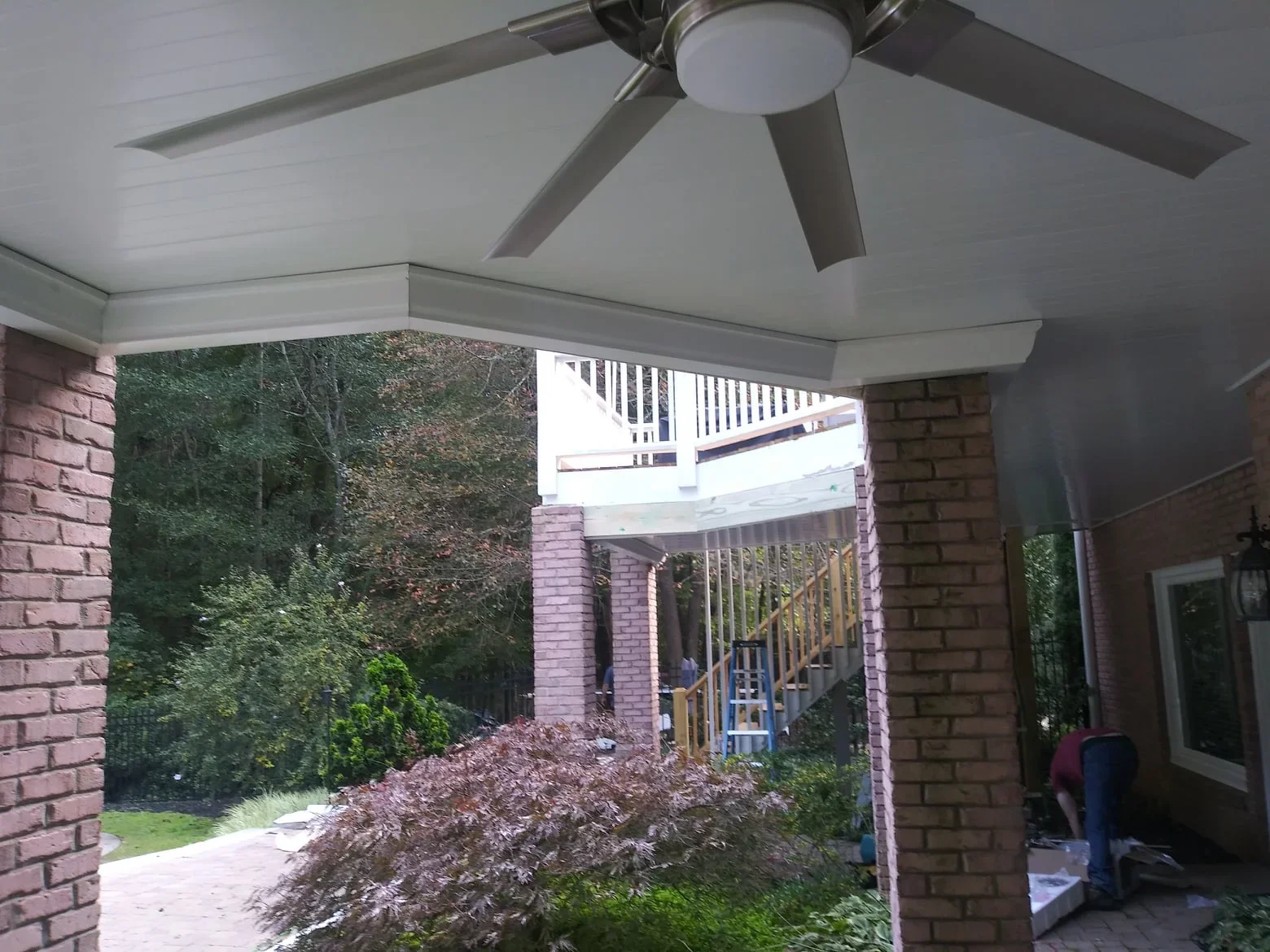 Under deck drainage system with finished ceiling, lighting, and ceiling fan beneath wooden deck