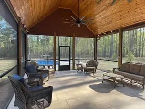 Spacious screened room with wood ceiling, ceiling fan, and lounge seating overlooking wooded area