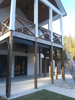 Two-story screen room with black metal railings, white columns, and elevated deck overlooking landscaped yard