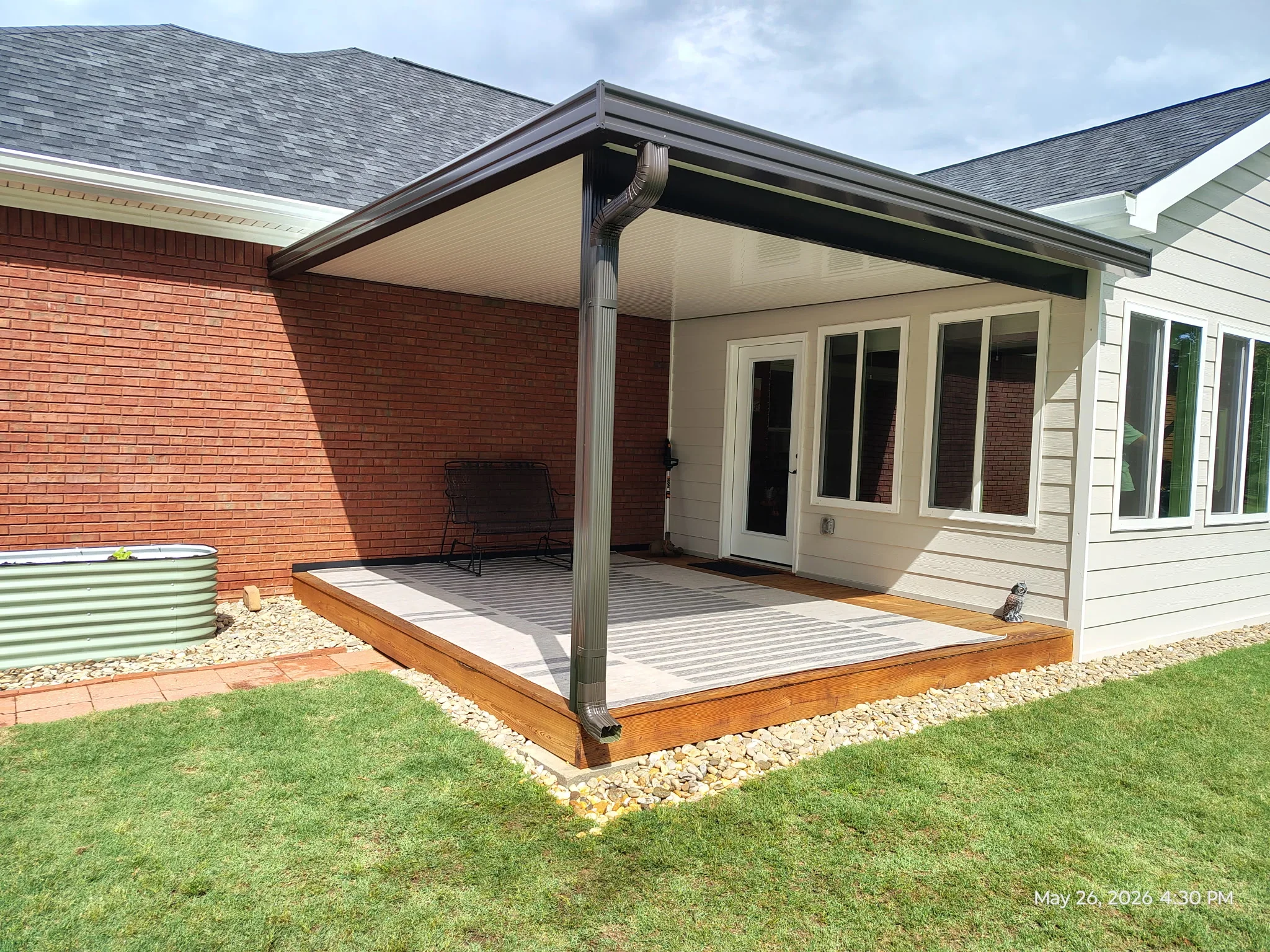 Aluminum patio cover with black frame and cream ceiling over composite deck with integrated drainage