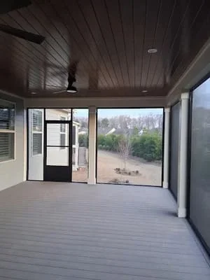 Covered screen room with dark frame, composite deck, and wooded view