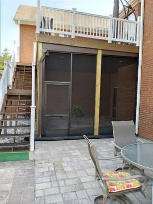 Bronze-framed screen room with sliding doors attached to brick home with paver patio