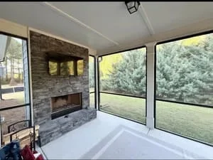 Bright screen room with large glass panels, stone fireplace wall, and views of green outdoor landscape