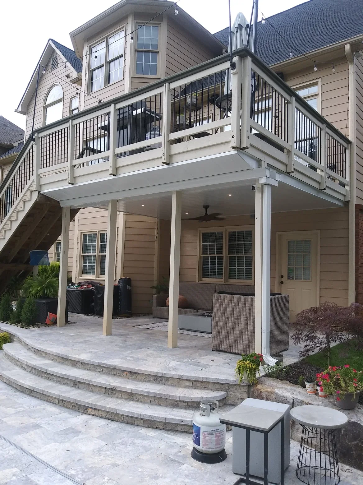 Under-deck drainage system with white posts, black railing, and paver patio below elevated deck