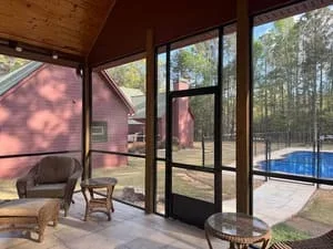 Black-framed screen room with pool view and wooden furniture